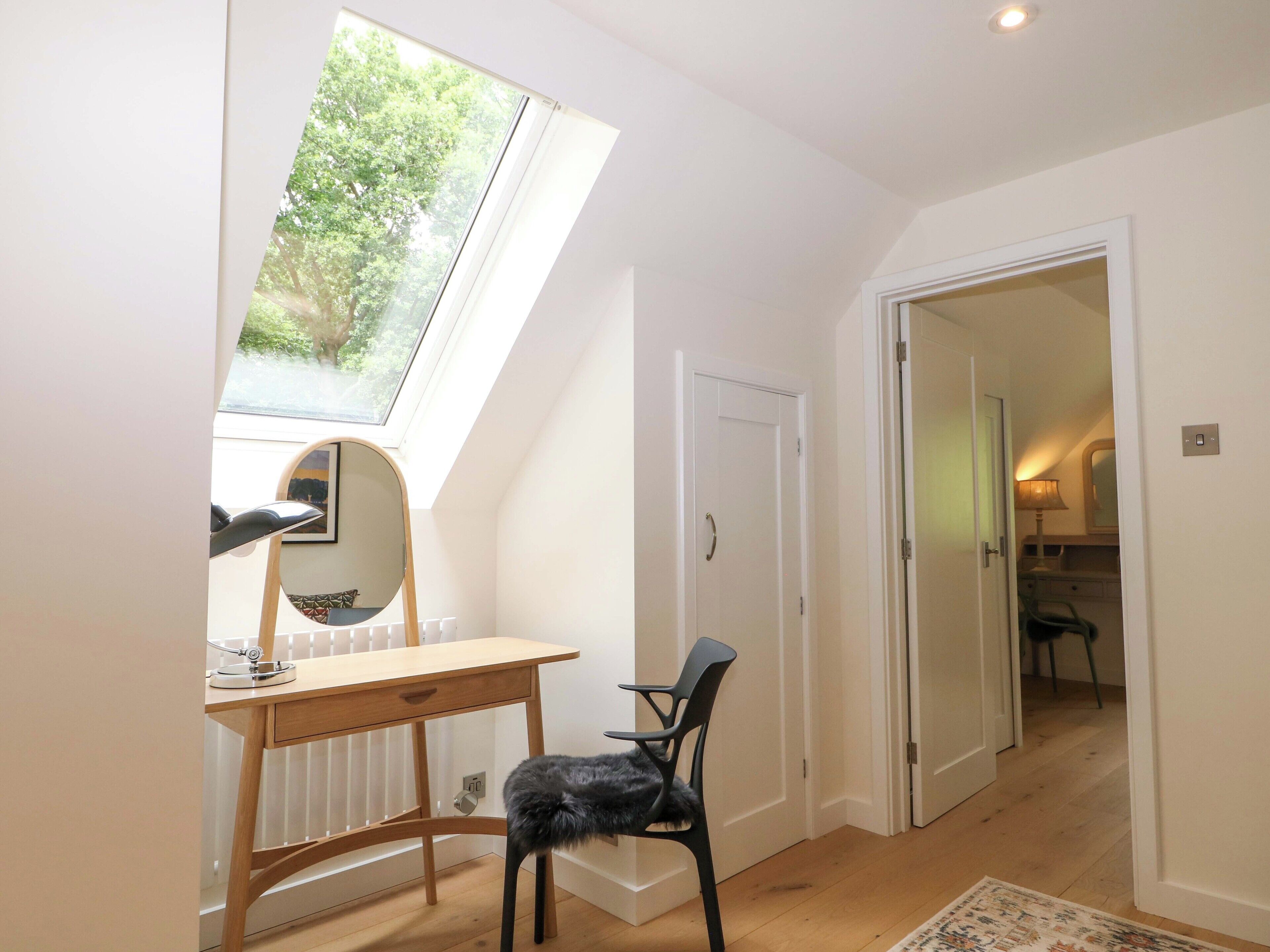 A room with a skylight, a desk with a chair, a radiator, and a door leading to another room.