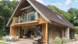 Una casa a due piani in legno con un balcone, una zona pranzo con mobili da esterno e una sedia sospesa.