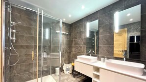 A modern bathroom with a glass-enclosed shower, two sinks, a large mirror, and a wooden door.