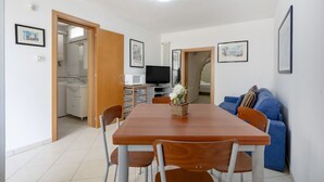 A dining area with a wooden table and chairs, a television, and a blue sofa. - GuestHost - Villa Belvedere: Apartment E (Ostuni)