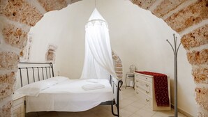 A bedroom with a bed under a white canopy, a dresser, a mirror, and a red patterned blanket. - GuestHost - Villa Belvedere: Apartment E (Ostuni)