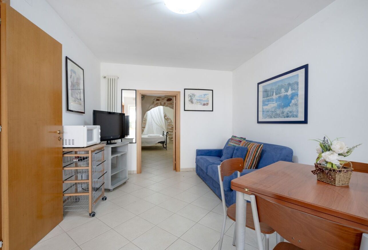 Una habitación con una televisión sobre un carrito, un sofá azul, una mesa de comedor y una cama con dosel.