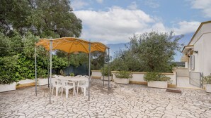 A patio with a table and chairs under a canopy, surrounded by planters and trees. - GuestHost - Villa Safi: Apartment A (Ostuni)