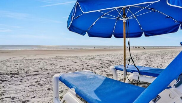 A beach scene with a blue umbrella and a lounge chair. - Modern In-Law Suite Near Jax Beaches & Mayo (Jacksonville)
