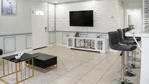 A modern living room with a flat-screen TV, a black sofa, a coffee table, and a bar area with stools. - Modern In-Law Suite Near Jax Beaches & Mayo (Jacksonville)