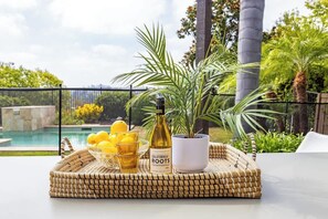 A wicker tray with a bottle of California Roots Chardonnay, a bowl of lemons, and glasses on a table with a view of a pool and greenery. - Private Hilltop Escape: Pool, Hot Tub, Near Beach (Vista)