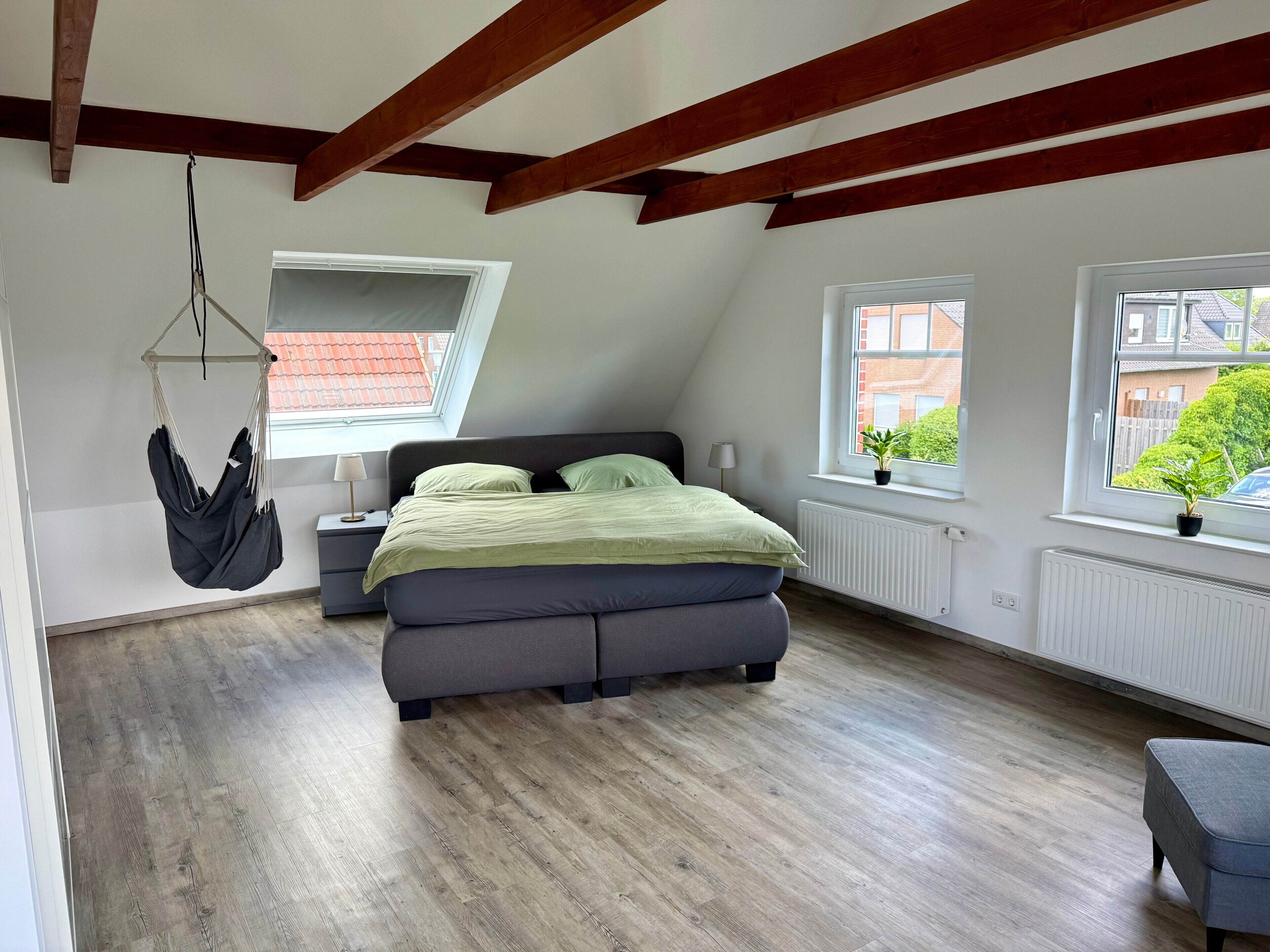 A bedroom with a bed, a hanging chair, two windows, and a radiator.