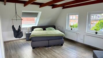 A bedroom with a bed, a hanging chair, two windows, and a radiator.