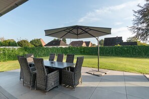 An outdoor patio with a table and chairs, a large umbrella, and a view of a residential area. - Holiday Home 'Neeborg' with Private Terrace, Garden, and Wi-Fi (Zetel)