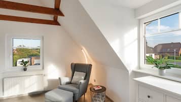 A modern loft bedroom with a sloped ceiling, a grey sofa, a bedside table with a lamp, and a view of a residential area.