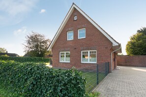 Et rødt murhus med saddeltag, en hoveddør og en lille forhave med en hæk.