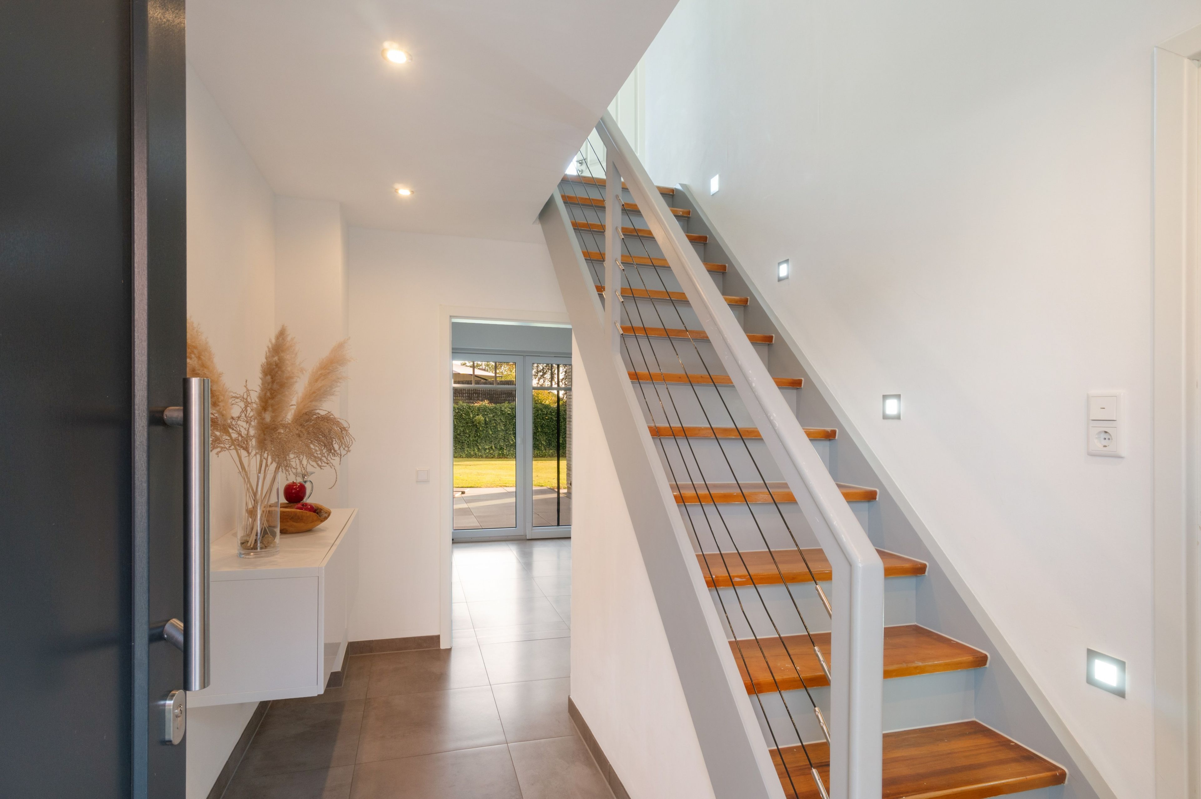 Un intérieur moderne avec un escalier, une porte et une vue à travers une porte vitrée.