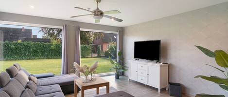 A modern living room with a sofa set, a flat-screen TV, and a ceiling fan.
