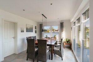 A dining area with a table and chairs, a window with curtains, and a door. - Holiday Home 'Neeborg' with Private Terrace, Garden, and Wi-Fi (Zetel)