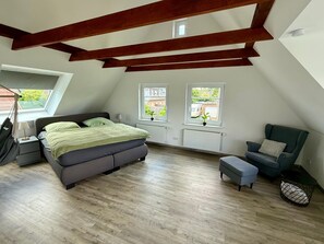 Quarto em estilo loft com cama, poltrona, mesa pequena e janela.