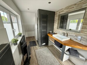 A modern bathroom with a large mirror, a wooden vanity, and a shower area. - Holiday Home 'Neeborg' with Private Terrace, Garden, and Wi-Fi (Zetel)