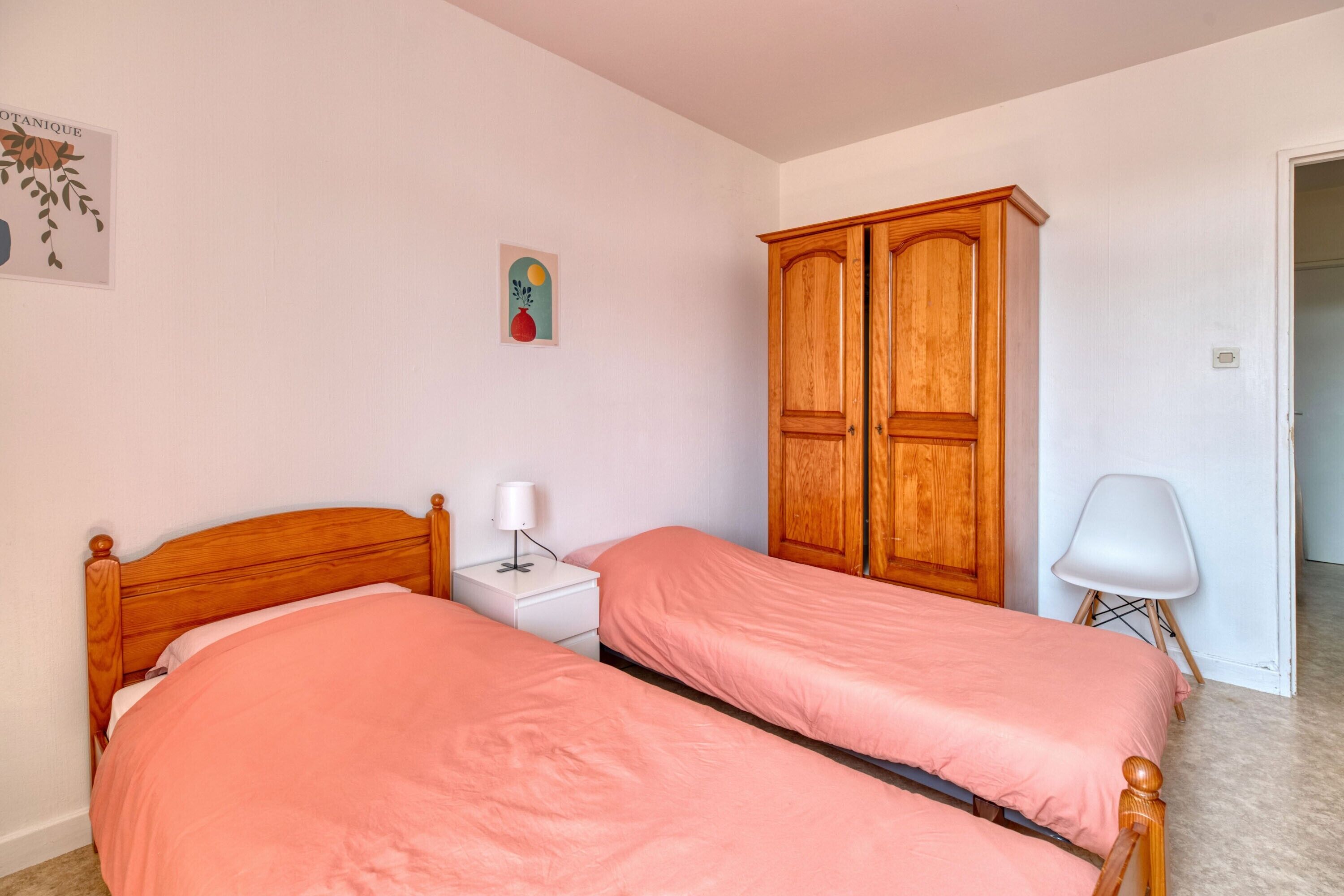 Un dormitorio con dos camas, un armario, una mesita de noche y una silla.
