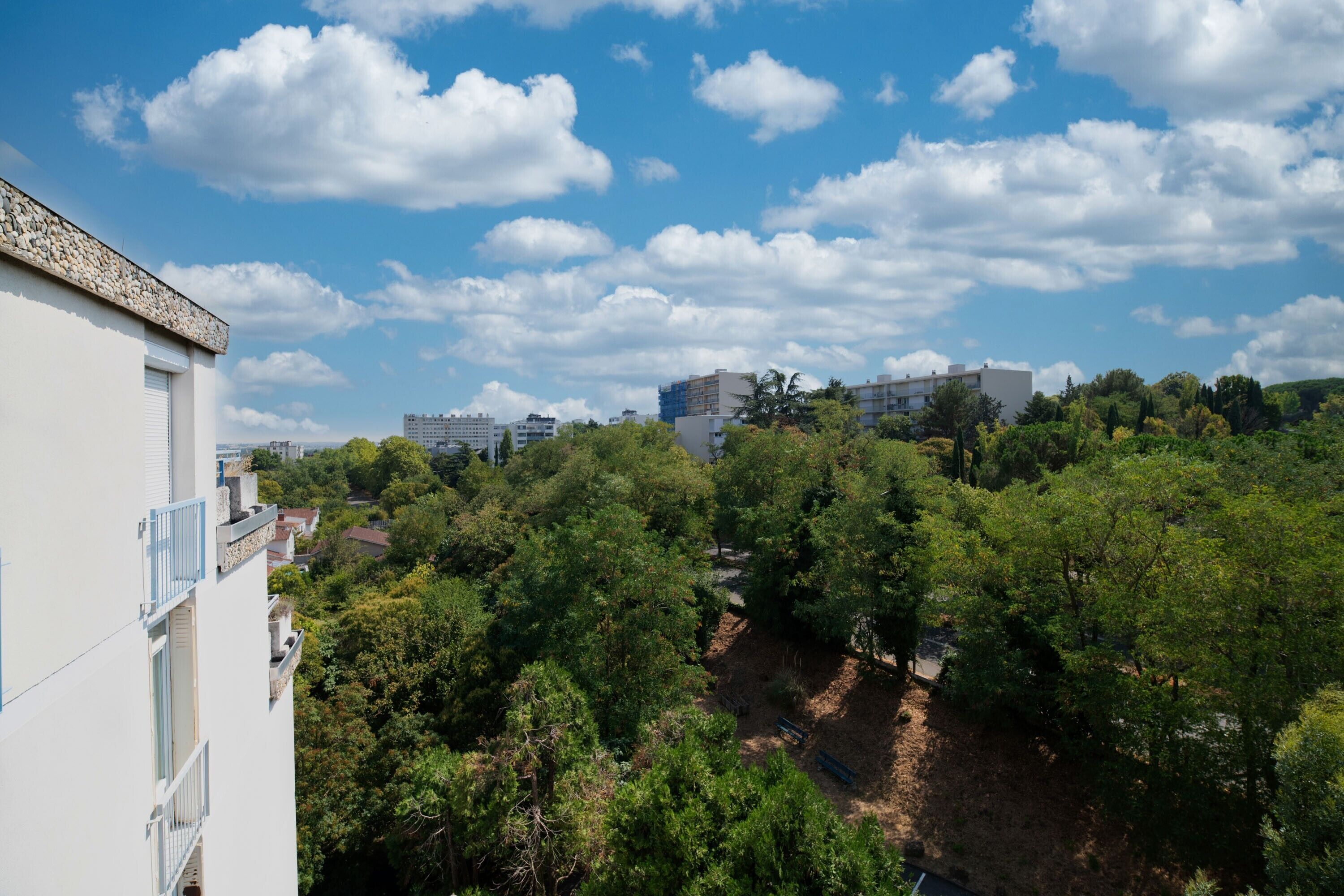 A residential area with a white building, a hill with trees, and a clear sky.