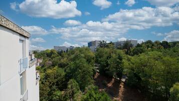 A residential area with a white building, a hill with trees, and a clear sky.