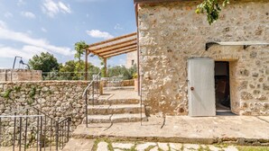 Ein Steinhaus mit einer Holzpergola, einer Treppe zu einer Tür und einer Steinsäule.