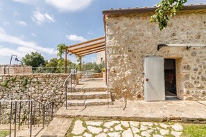 A stone building with a wooden pergola, a staircase leading to a door, and a stone wall.