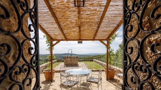 Eine Terrasse im Freien mit Tisch, Stühlen, einer Pergola und einer Steinmauer.