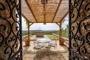 An outdoor patio with a table and chairs, a pergola, and a stone wall.