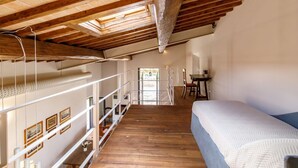 Ein Schlafzimmer mit Holzbalkendecke, einem Bett, einem Schreibtisch und einer Treppe zu einer erhöhten Ebene.