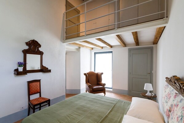 A bedroom with a lofted area, a bed, a chair, a mirror, and a door.