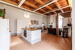 Une cuisine spacieuse avec un parquet disposé en motif à chevrons, des poutres en bois au plafond et un îlot central doté d’un évier et d’un plan de travail.