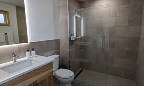 A modern bathroom with a glass shower enclosure, a white sink with a wooden vanity, and a toilet.