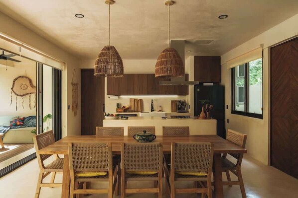 A modern kitchen with wooden cabinets, a central island, and hanging wicker pendant lights. - Perfect for 10 Guests w/ Rooftop & Jungle Views (Tulum)