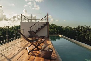 A wooden deck with a pool, a staircase, and lounge chairs.