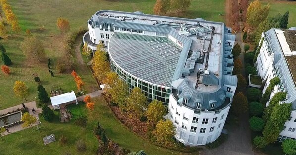 Un edificio grande y circular con techo de vidrio, rodeado de un césped cuidado y árboles.