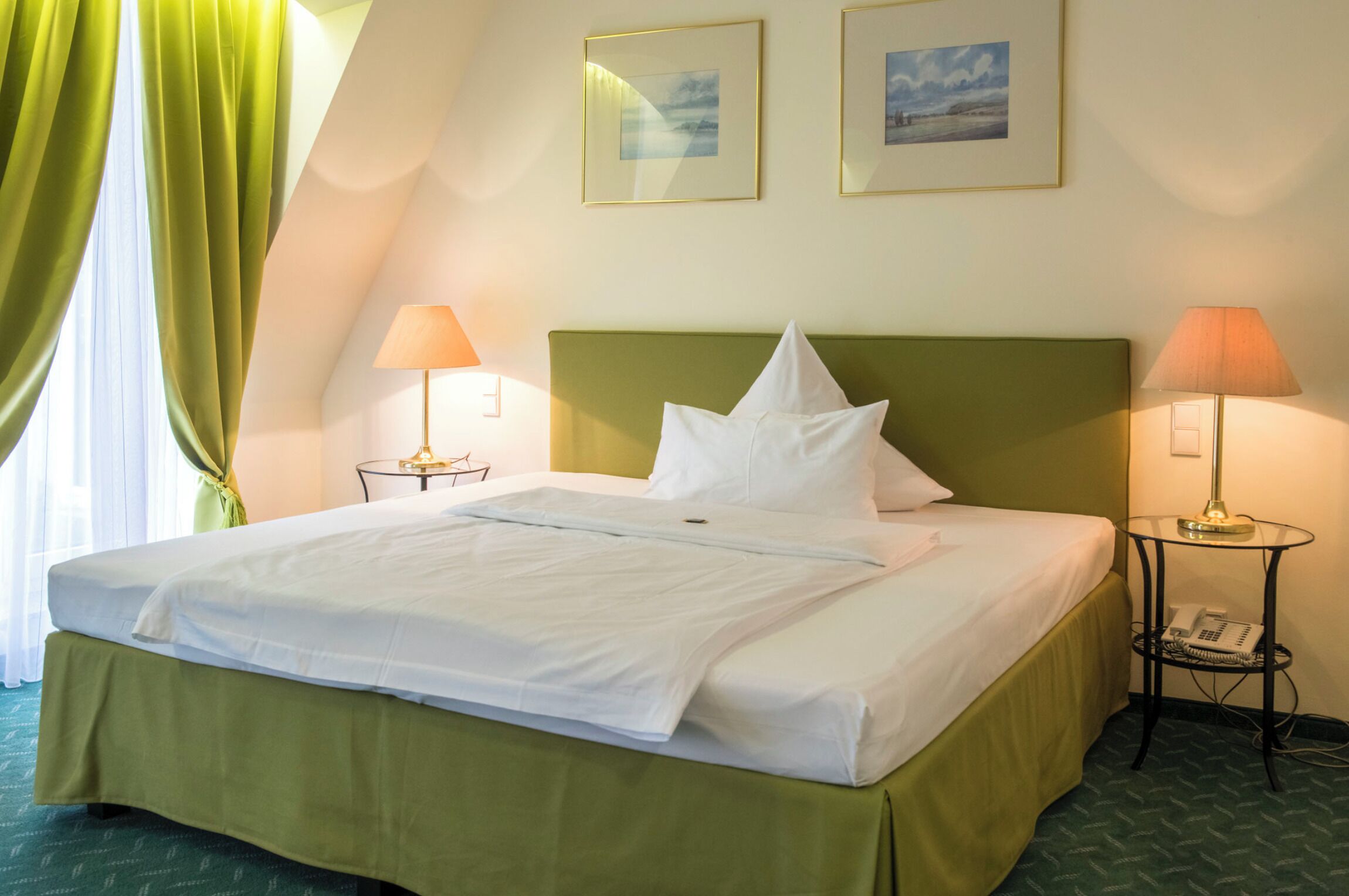 A neatly made bed with white linens, a green headboard, and two bedside lamps.