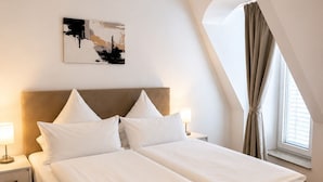 A double bed with a headboard, a bedside table with a lamp, a wall-mounted artwork, and a window with curtains. - Hotel Artrium am Park (Dietzenbach)