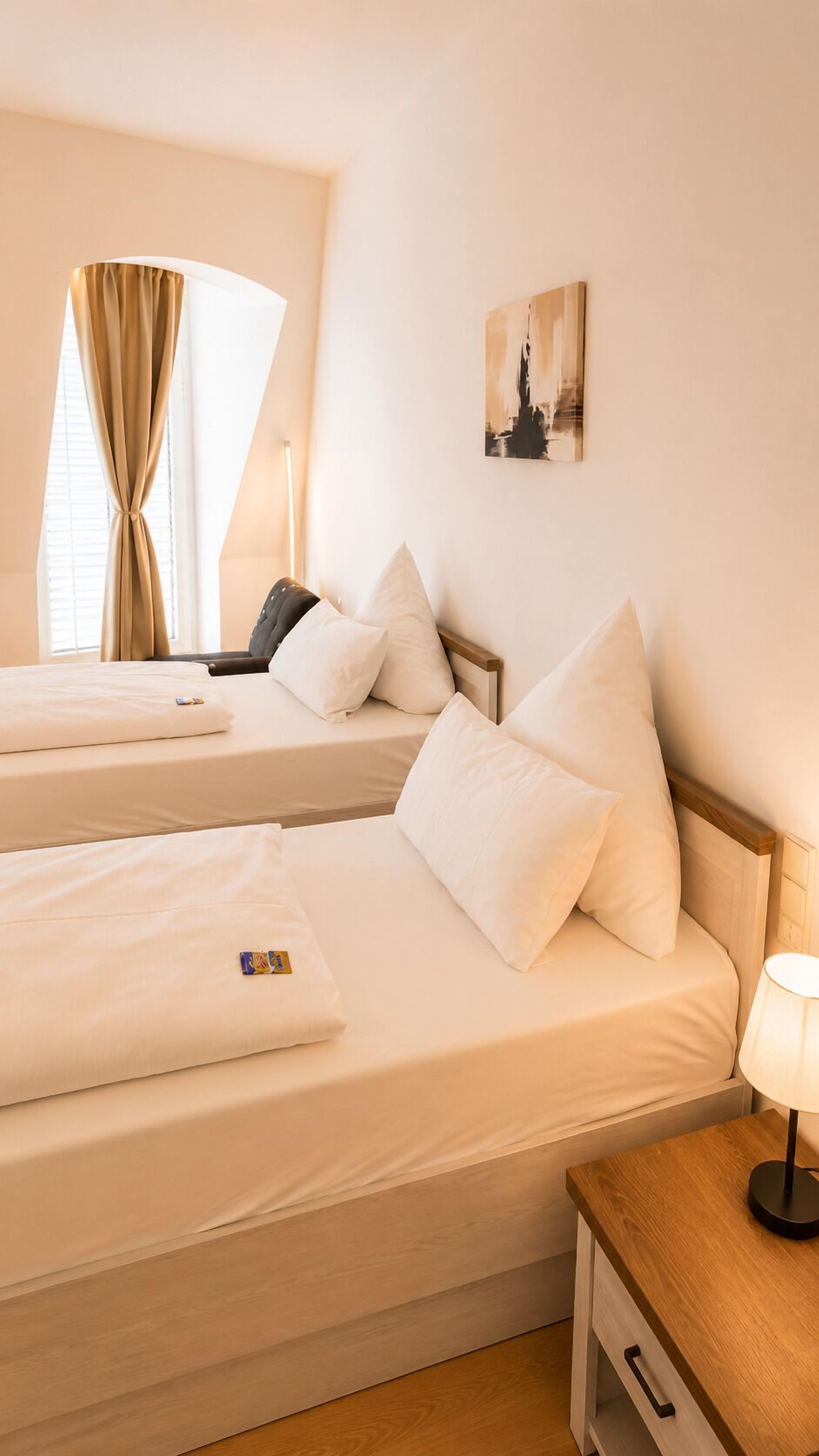 A hotel room with two beds, a nightstand, a lamp, and a painting on the wall.