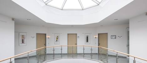 Interior moderno com guarda-corpo de vidro, claraboia central e portas numeradas.