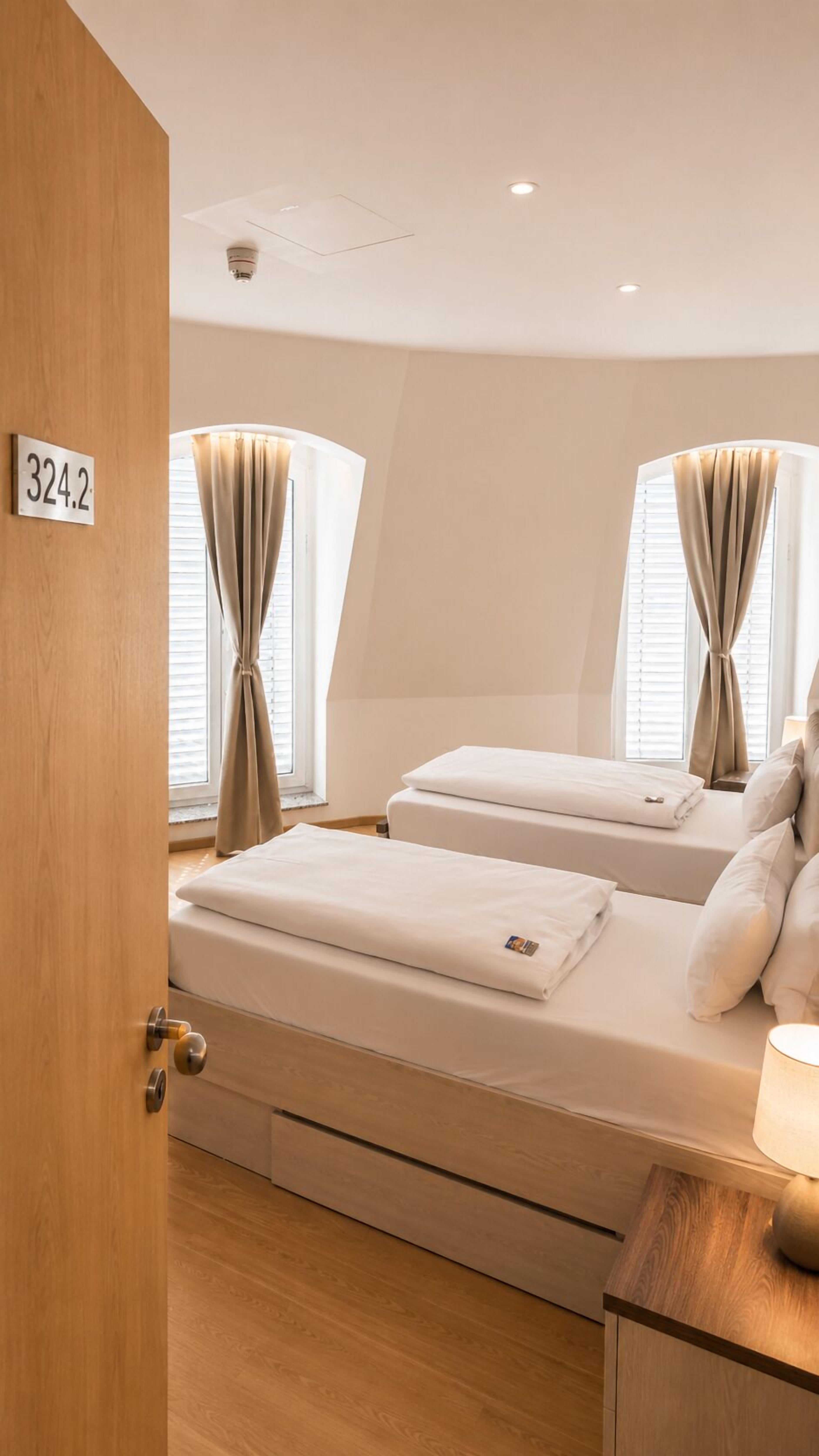 Habitación de hotel con dos camas, una puerta de madera y un cartel con número.