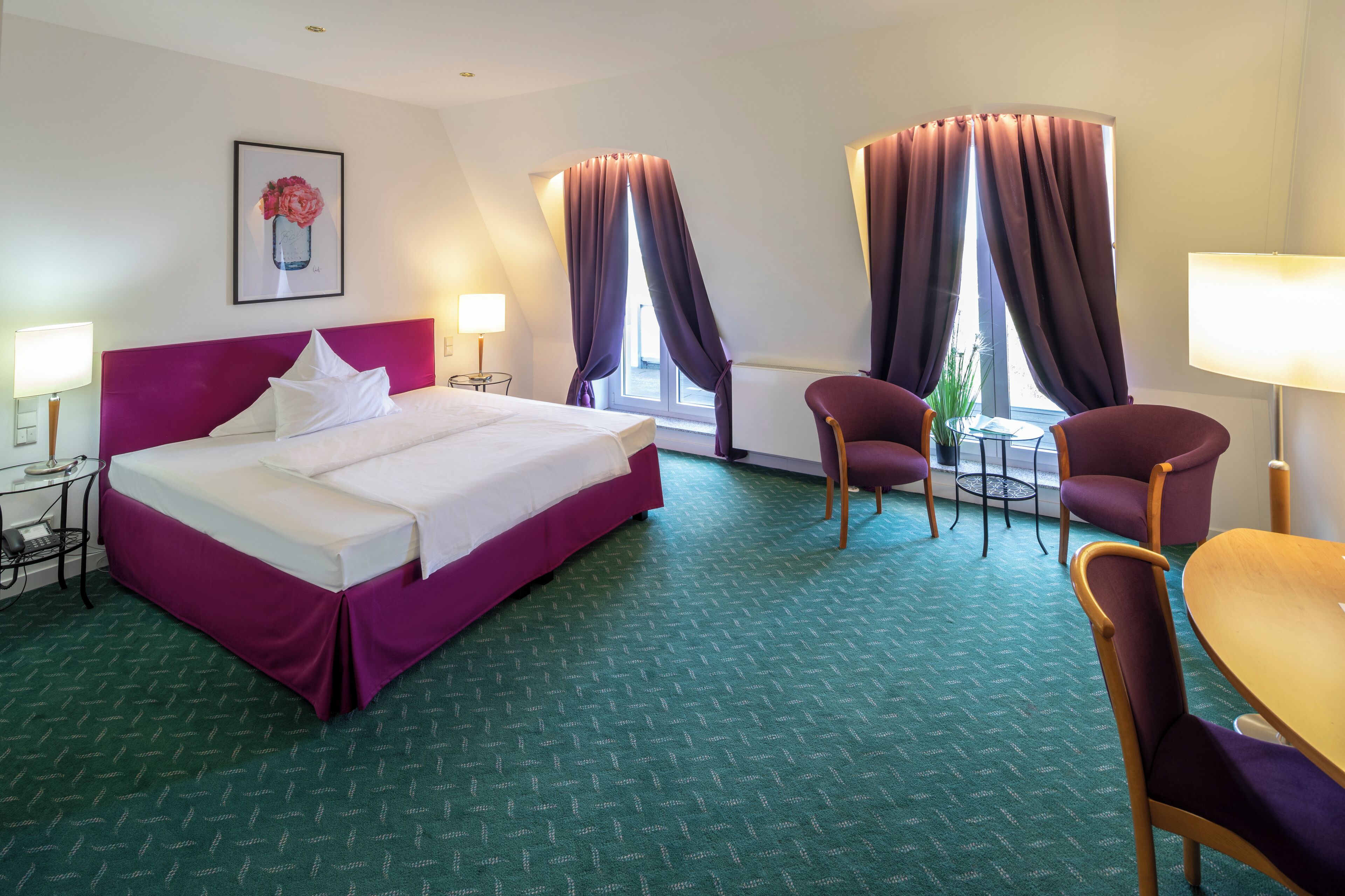 Una habitación de hotel con una cama, dos sillas, una mesita, una lámpara y una ventana con cortinas.