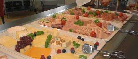Un bufé con diversos quesos, carnes y frutas.