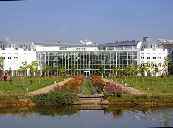 A modern building with a glass facade, surrounded by a well-maintained garden and a small pond.