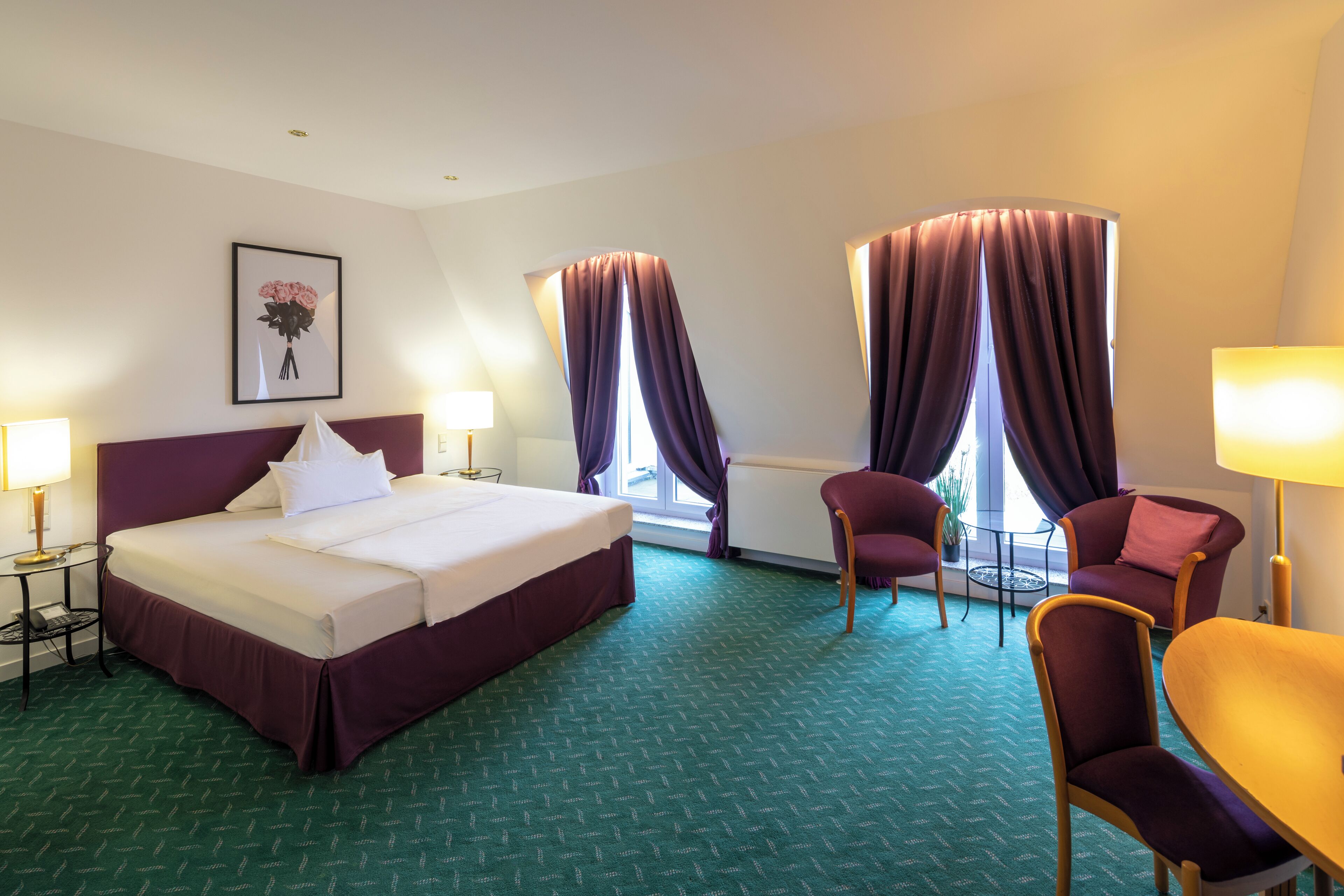 Una habitación de hotel con una cama grande, dos sillas, una mesita y un ventanal con cortinas.