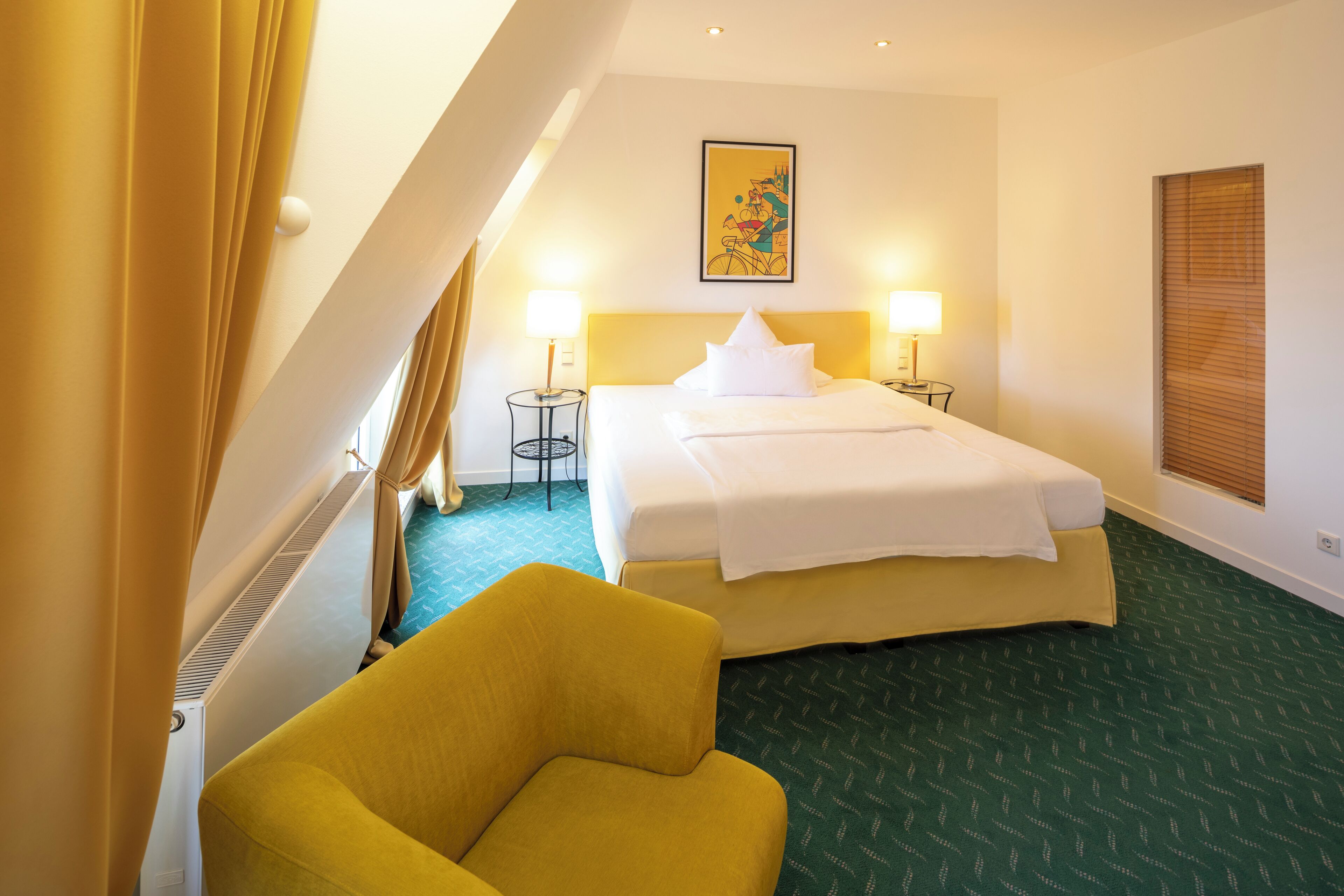 A hotel room with a bed, two bedside lamps, a chair, a radiator, and a window with blinds.