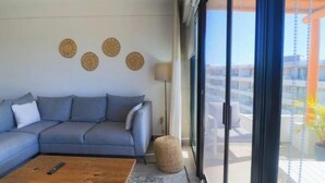 Een moderne woonkamer met een grijze bank, een houten salontafel en een groot raam met uitzicht op de stad.