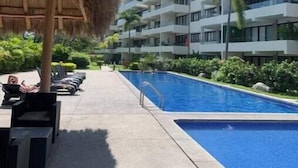 Een resort met een zwembad, ligbedden en een dak van riet.