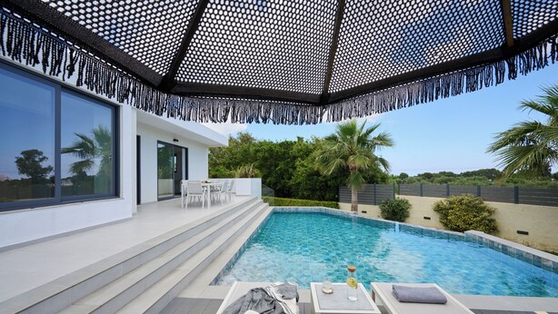 A modern outdoor pool area with a covered seating area, steps leading to a pool, and a view of the surrounding greenery.