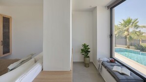 A modern room with a large window, a bed with a view of a swimming pool, a potted plant, and a bench with a book.