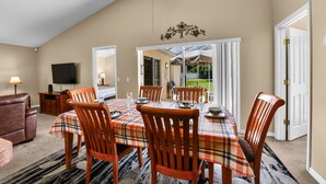 A dining area with a table set for six, surrounded by wooden chairs, a ceiling fan, and a television on the wall.
