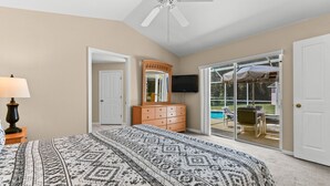 A bedroom with a large bed, a dresser, a TV, and a sliding glass door leading to an outdoor patio.